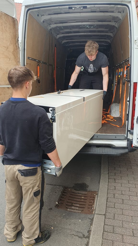 Mitarbeiter von Lünekurier tragen einen Kühlschrank in einen Transporter